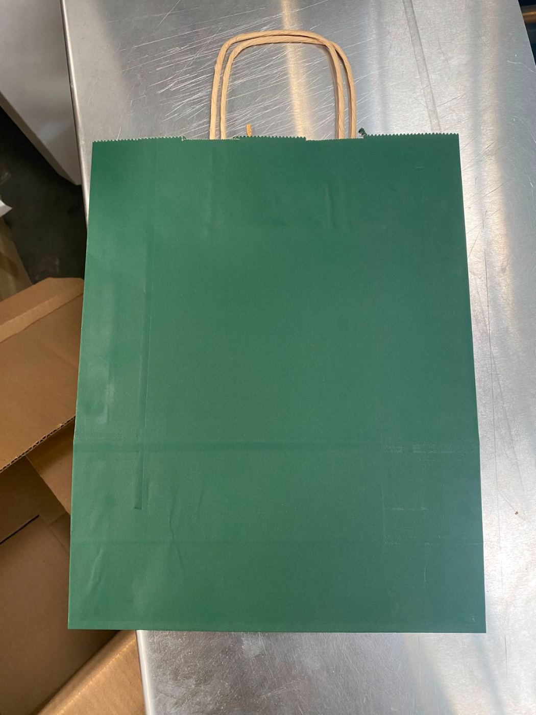 Échantillon réel de sac kraft teinté vert bouteille, poignées torsadées, posé sur la table de l'atelier